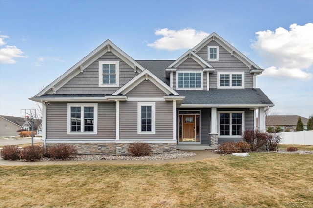 craftsman house with stone siding, roof with shingles, a front yard, and fence