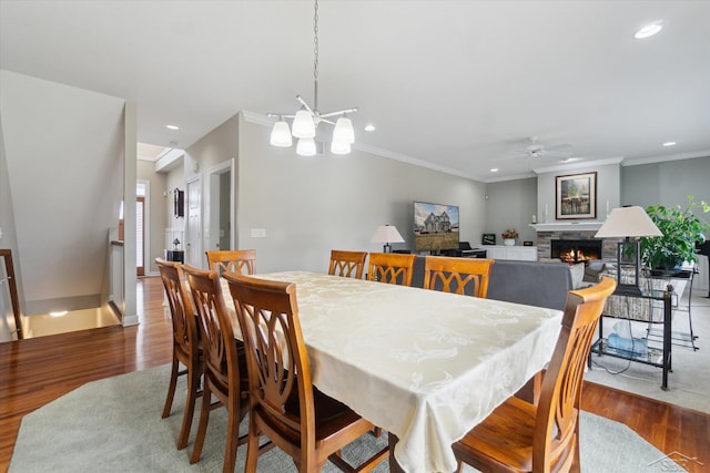 dining space featuring a stone fireplace, recessed lighting, wood finished floors, and ornamental molding