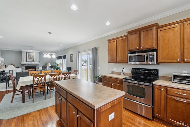 kitchen with brown cabinets, a kitchen island, a warm lit fireplace, open floor plan, and appliances with stainless steel finishes