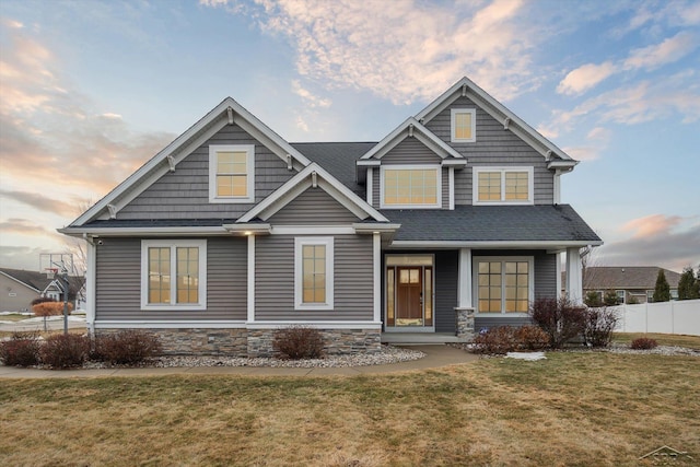 craftsman house with a yard, stone siding, and fence