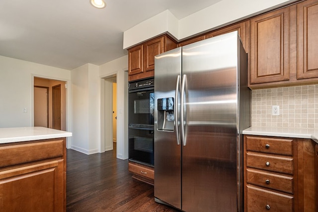 kitchen with dark wood-type flooring, decorative backsplash, brown cabinets, stainless steel fridge, and dobule oven black