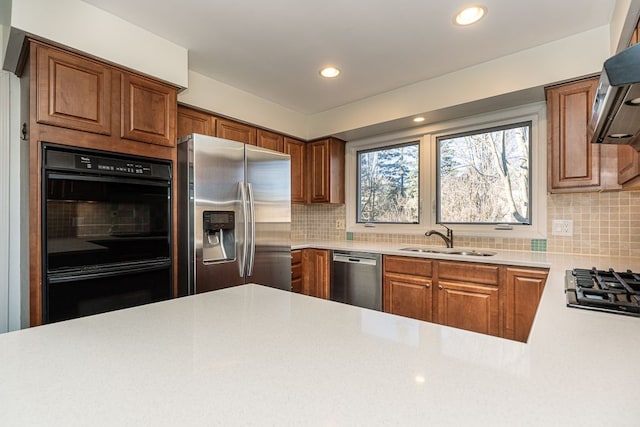 kitchen with black appliances, a sink, tasteful backsplash, wall chimney exhaust hood, and light countertops