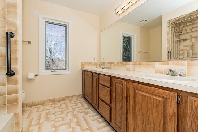 full bathroom featuring double vanity, visible vents, a tile shower, and a sink