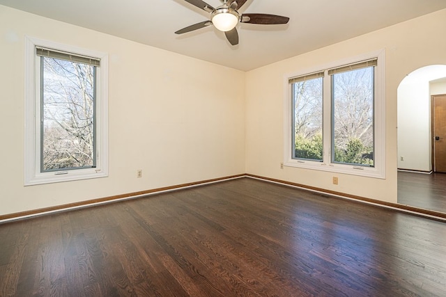 empty room featuring baseboards, arched walkways, a healthy amount of sunlight, and dark wood finished floors