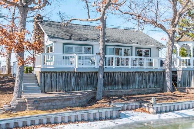 view of front of house featuring stairway, roof with shingles, a deck, and a chimney