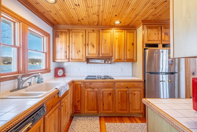 kitchen featuring tile countertops, dishwashing machine, a sink, and freestanding refrigerator