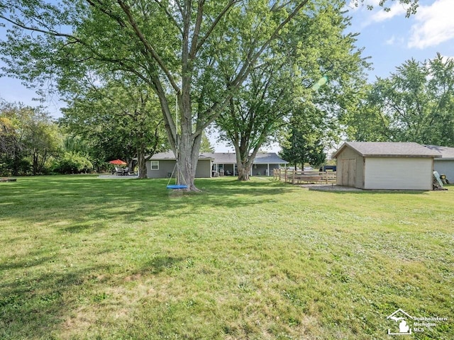 view of yard with a trampoline, an outdoor structure, and fence