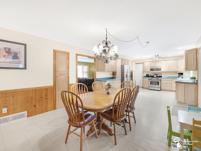 dining room with visible vents, a wainscoted wall, wood walls, light floors, and a notable chandelier