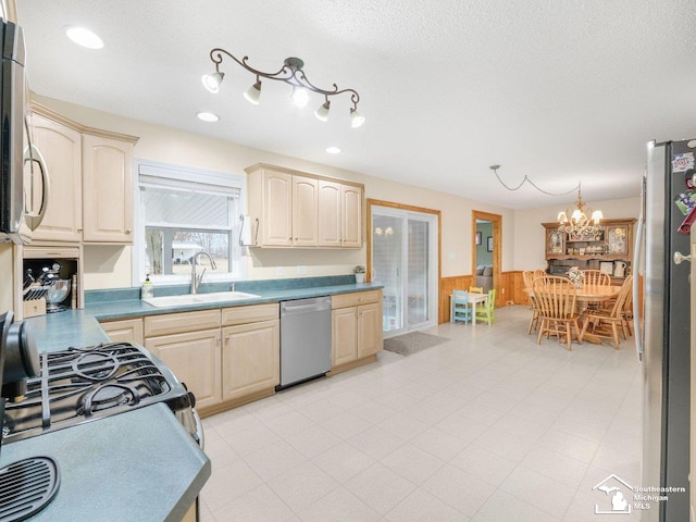 kitchen featuring a sink, a textured ceiling, appliances with stainless steel finishes, wood walls, and wainscoting