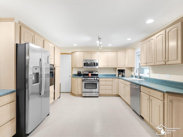 kitchen with dark countertops, light brown cabinets, recessed lighting, appliances with stainless steel finishes, and a sink