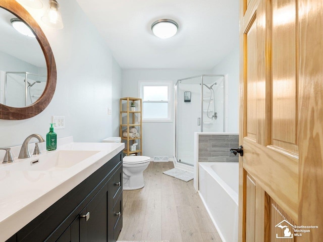 bathroom featuring vanity, toilet, wood finished floors, and a stall shower