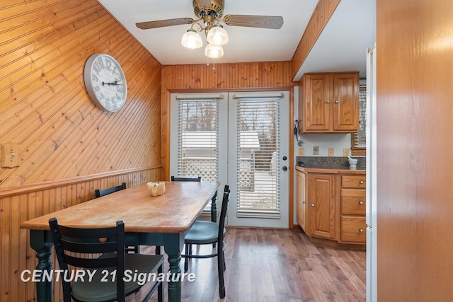 dining space featuring light wood finished floors, wooden walls, and ceiling fan