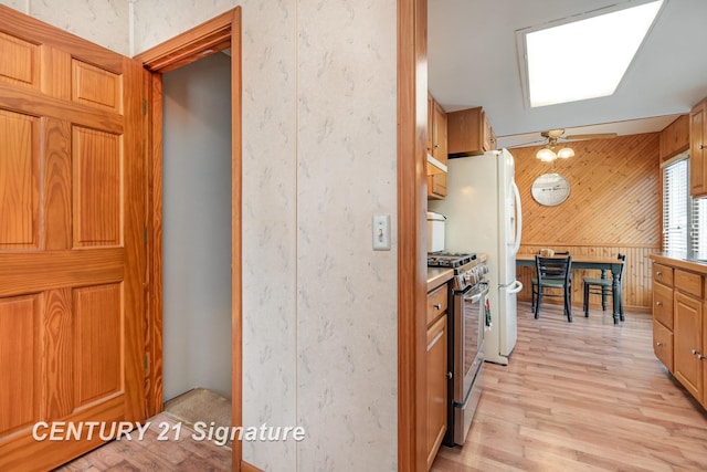 kitchen featuring wooden walls, brown cabinetry, light wood-style flooring, light countertops, and stainless steel gas range oven