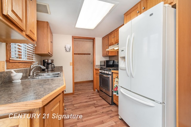 kitchen with under cabinet range hood, gas range, white refrigerator with ice dispenser, light wood-style floors, and a sink