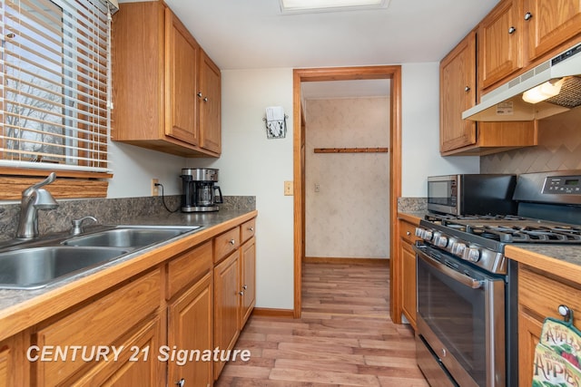 kitchen with a sink, under cabinet range hood, light wood-style floors, appliances with stainless steel finishes, and brown cabinetry