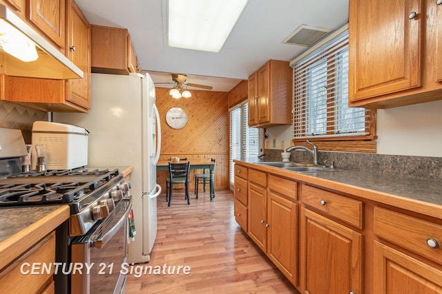 kitchen featuring dark countertops, wooden walls, under cabinet range hood, stainless steel gas range, and a sink