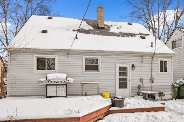 snow covered house featuring cooling unit and a chimney