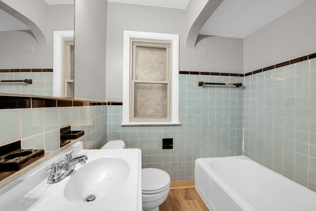 5984 Courville St, Detroit, MI 48224 - bathroom featuring toilet, wainscoting, wood finished floors, tile walls, and a sink