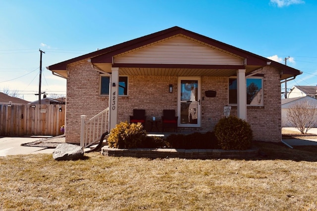 view of front of property with brick siding, covered porch, a front lawn, and fence