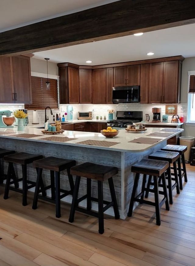 kitchen featuring beam ceiling, light wood-style flooring, stainless steel microwave, black gas range oven, and a breakfast bar area