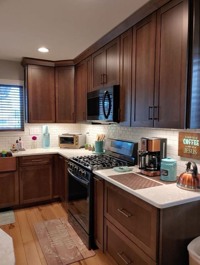 kitchen with black range with gas cooktop, light wood finished floors, tasteful backsplash, and light countertops