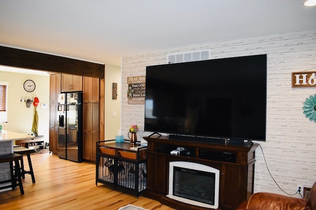 living room with light wood finished floors, a glass covered fireplace, and wood walls