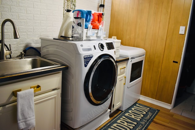 laundry area featuring a sink, wood finished floors, cabinet space, and washing machine and clothes dryer