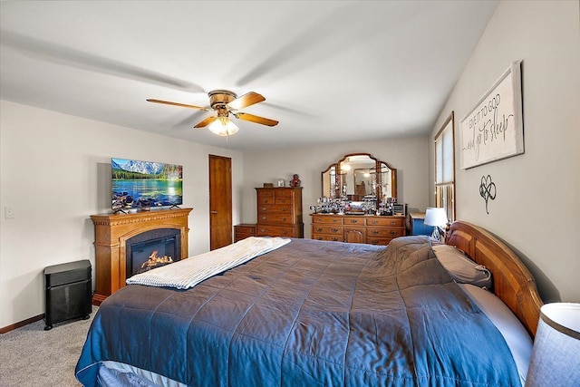 carpeted bedroom with a glass covered fireplace, baseboards, and ceiling fan