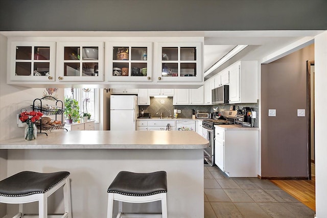 kitchen featuring a peninsula, backsplash, glass insert cabinets, and appliances with stainless steel finishes