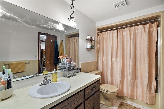 full bath with visible vents, toilet, tile walls, wainscoting, and vanity