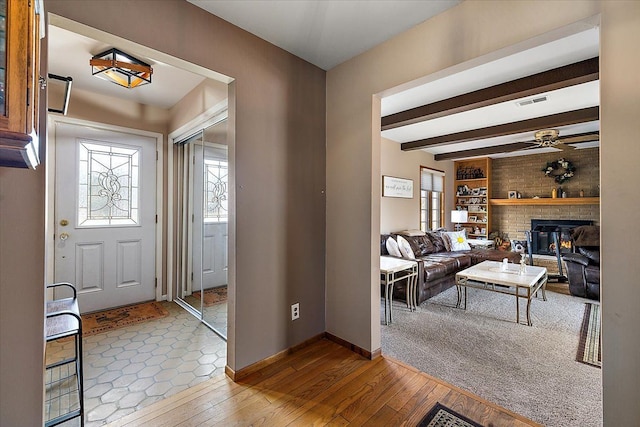 foyer featuring beamed ceiling, visible vents, hardwood / wood-style flooring, a fireplace, and baseboards