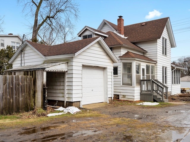 view of front facade featuring a garage, roof with shingles, a chimney, and fence