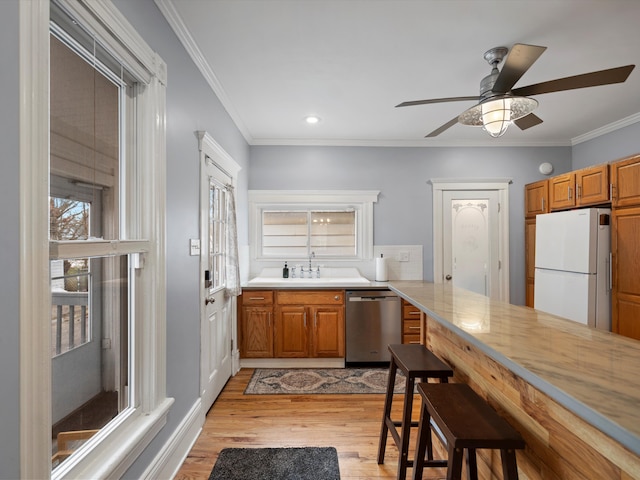 kitchen with a sink, freestanding refrigerator, crown molding, light wood finished floors, and dishwasher