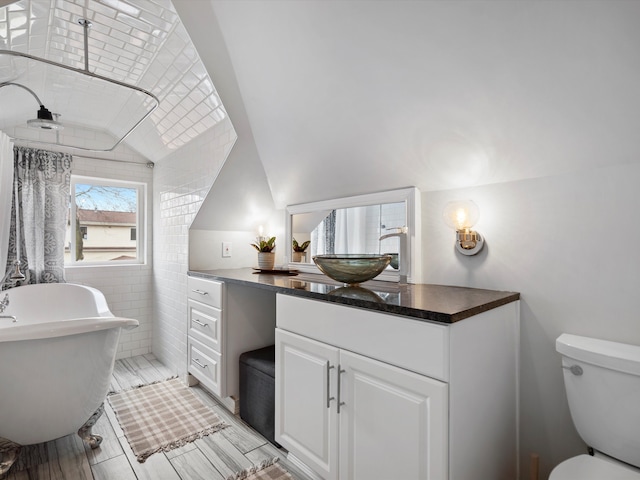 bathroom featuring lofted ceiling, a soaking tub, vanity, and toilet