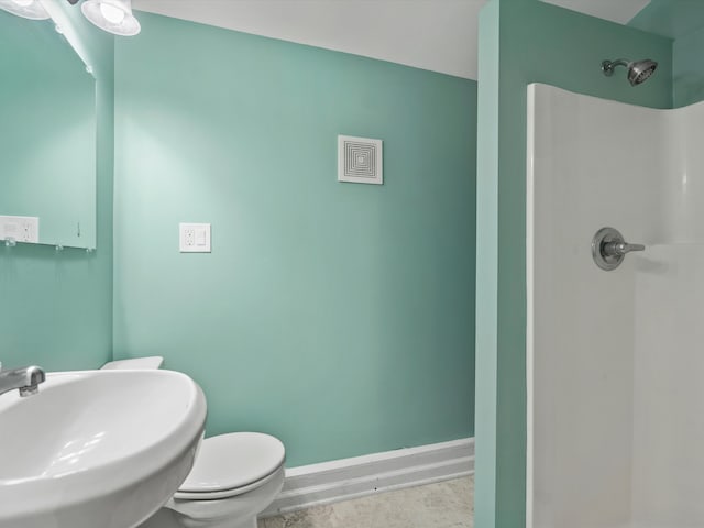 bathroom featuring toilet, a shower, baseboards, and a sink