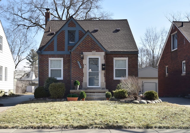 tudor home with a front lawn, brick siding, an outdoor structure, and a chimney