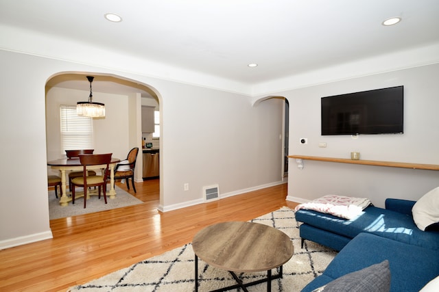 living area featuring arched walkways, visible vents, light wood-style flooring, and recessed lighting