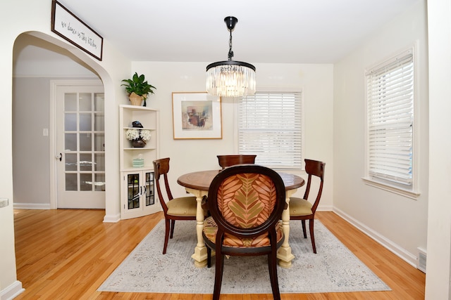 dining room with arched walkways, a healthy amount of sunlight, and light wood-style floors