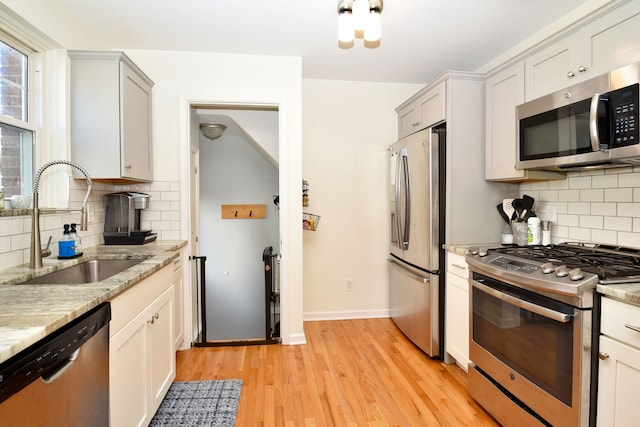 kitchen featuring a sink, light stone counters, tasteful backsplash, appliances with stainless steel finishes, and light wood finished floors