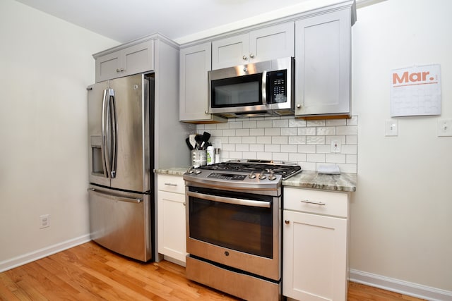 kitchen with backsplash, gray cabinetry, light stone countertops, appliances with stainless steel finishes, and light wood-style floors