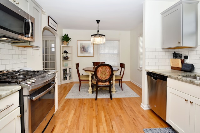 kitchen with decorative light fixtures, backsplash, appliances with stainless steel finishes, and light wood-style flooring