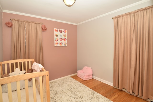 bedroom featuring light wood-type flooring, baseboards, a nursery area, and crown molding