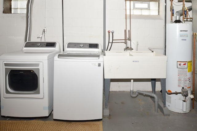 clothes washing area featuring laundry area, separate washer and dryer, water heater, and a sink