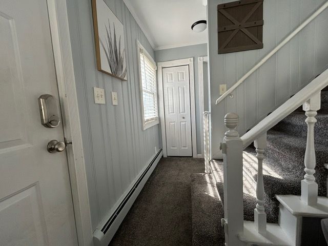 doorway featuring stairs, baseboard heating, ornamental molding, and dark carpet