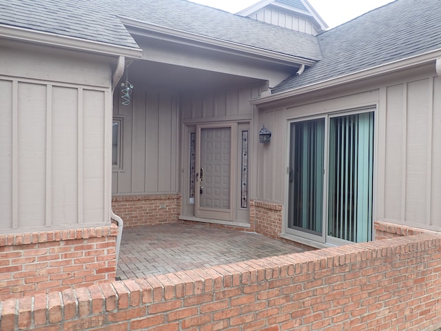 entrance to property with board and batten siding, brick siding, and roof with shingles