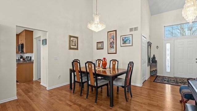 dining area with visible vents, light wood-style flooring, a towering ceiling, baseboards, and a chandelier