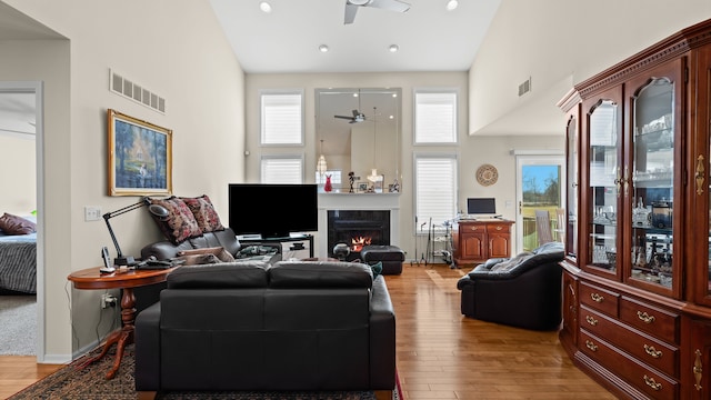 living room with a high end fireplace, visible vents, ceiling fan, high vaulted ceiling, and wood-type flooring