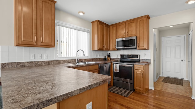 kitchen with dark countertops, decorative backsplash, appliances with stainless steel finishes, wood finished floors, and a sink