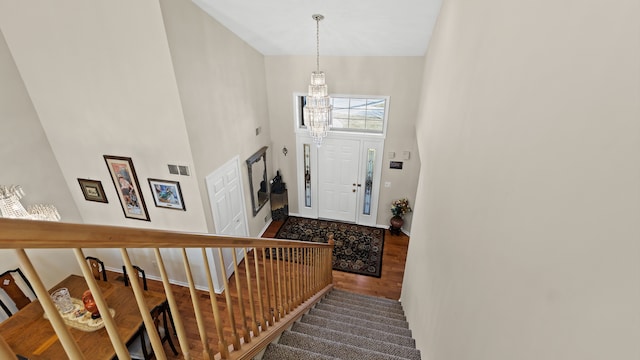 foyer with visible vents, a notable chandelier, wood finished floors, a high ceiling, and stairs