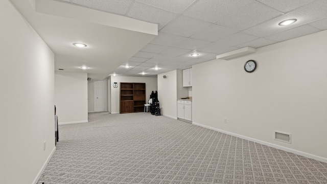 finished below grade area with a paneled ceiling, visible vents, light carpet, and baseboards